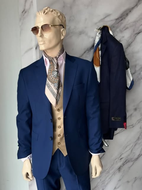 Maniquí en el local con traje azul, chaleco camel y pañuelo estampado al cuello, junto a un saco azul colgado.
