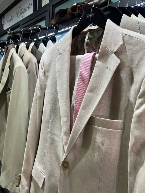 Percha con sacos en tonos claros y una corbata rosa.